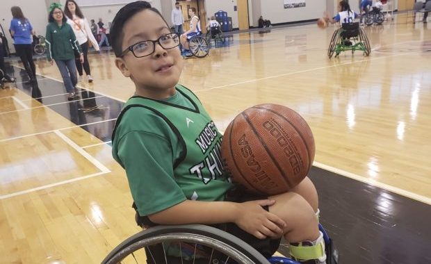 Chuy sitting in his wheelchair on a basketball court holding a basketball