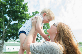 Mom and son outside. Son raised in air by mother.