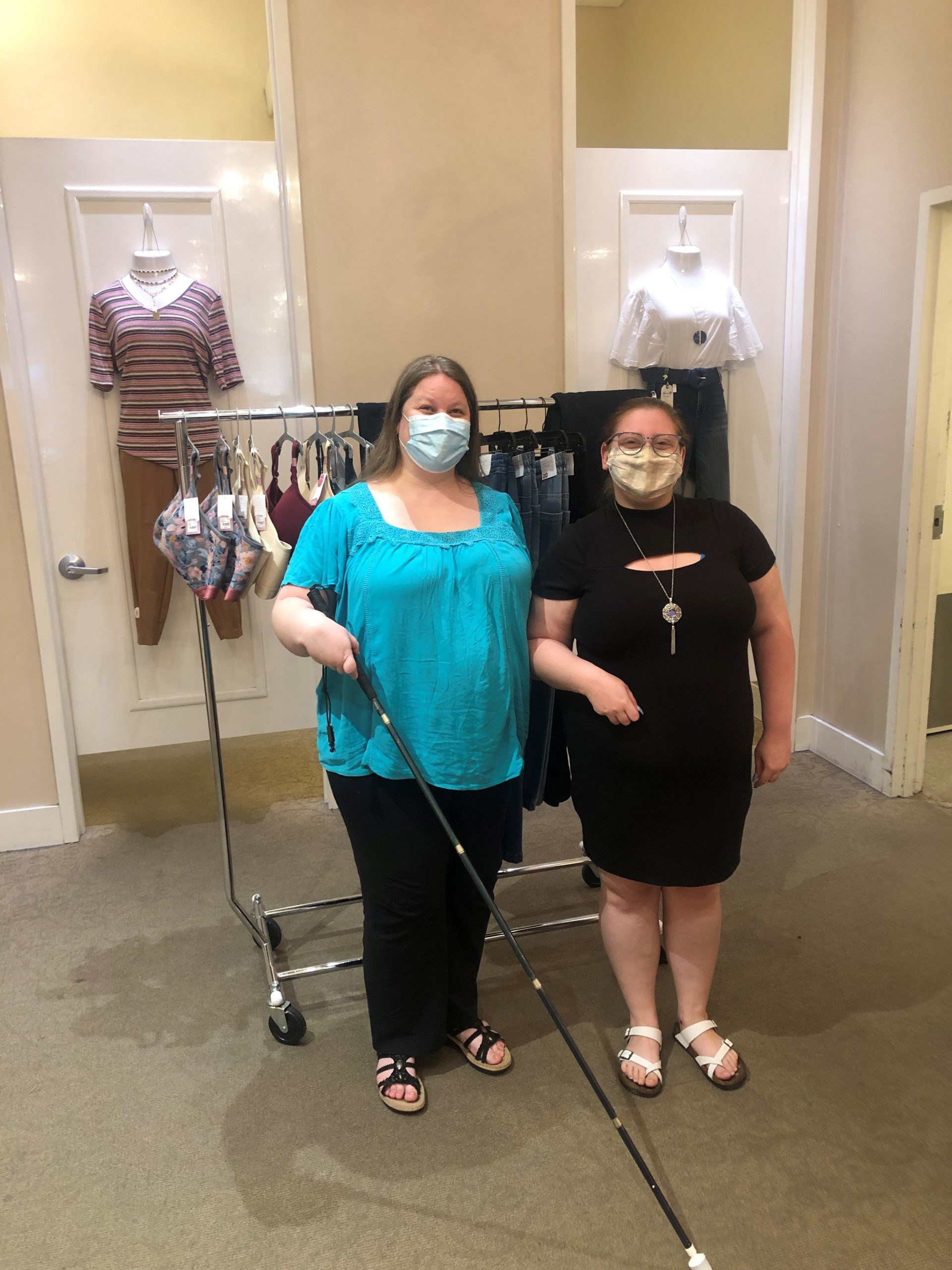 Picture of two people, one appears to be visually impaired the other is holding her arm up and appears to be assisting the person holding the cane.