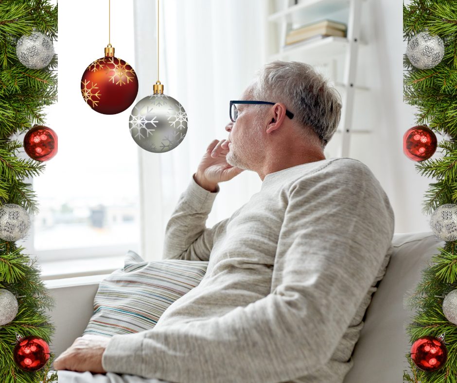 Image of aging adult in all white staring out of a window. holiday decorations are the border of the image. A red and silver ornament hangs from top of image in front of person.