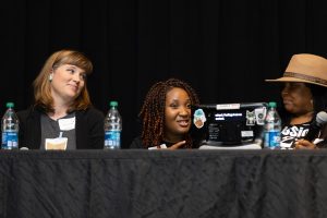 Image of a panel of three people. Person to the left and right are looking at the person in the center speaking.