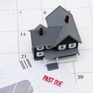 A small model house placed on a calendar page, next to an envelope stamped with the words “PAST DUE” in red letters, symbolizing overdue rent or mortgage payments.Would you like me to create a shorter version (under 125 characters) for accessibility, or keep this detailed version for context?