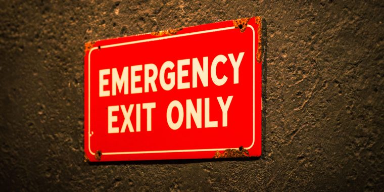 Close-up of a red sign mounted on a dark wall that reads, “Emergency Exit Only.”